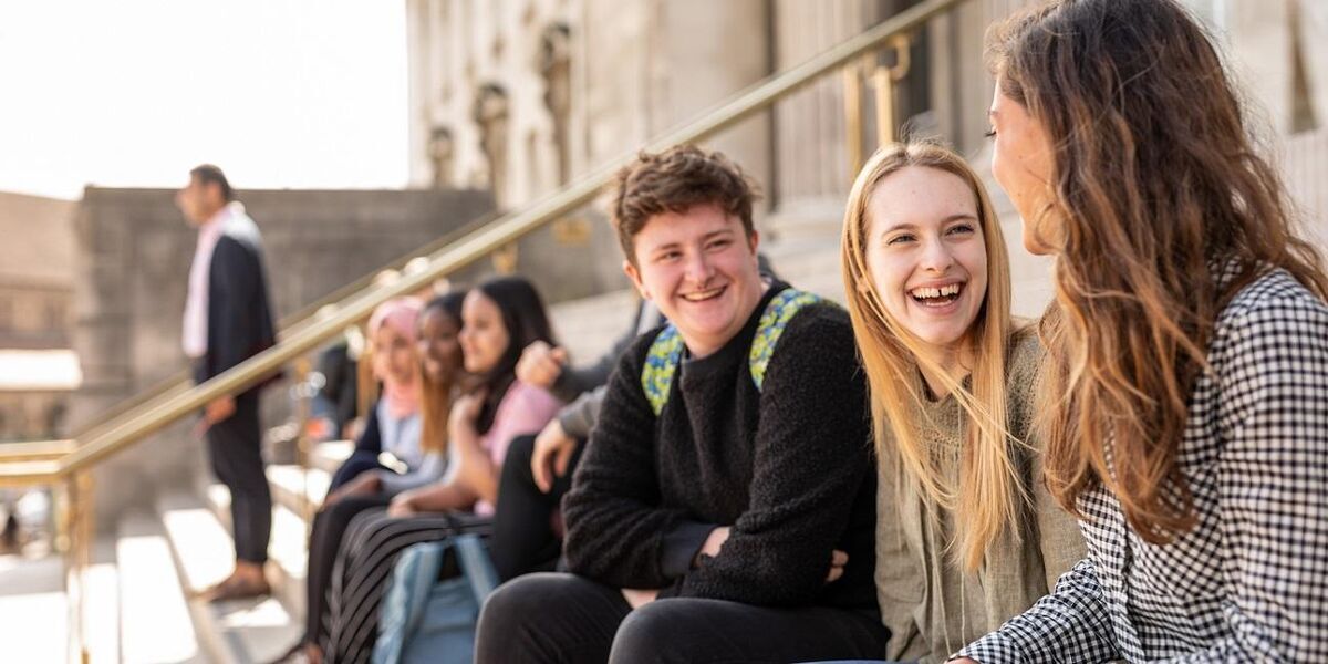 A group of students sitting on the steps in front of the Parkinson Building, chatting and laughing