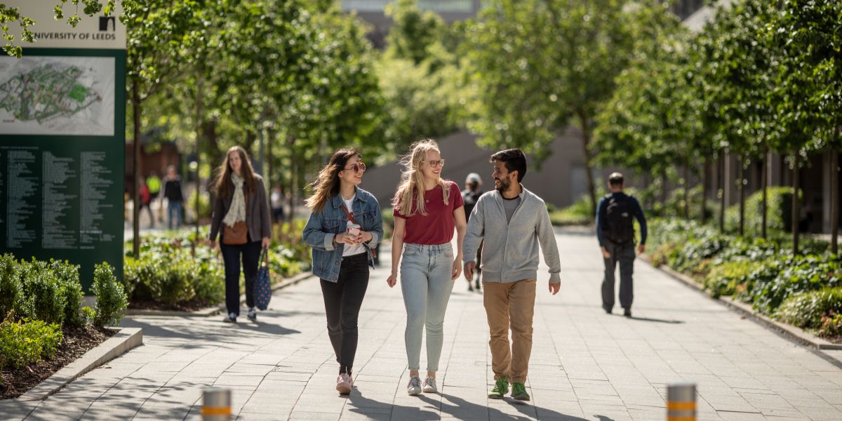 Three students walk in a line towards the camera, they are looking at each other and smiling.