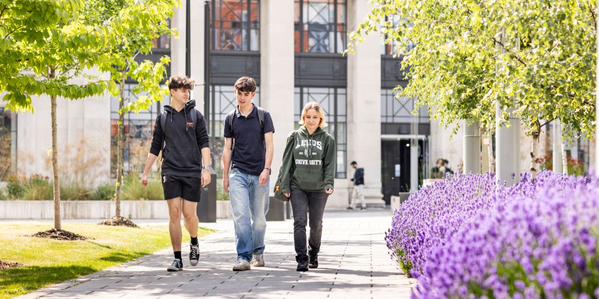 A group walking together along a path lined with trees and vibrant purple flowers.