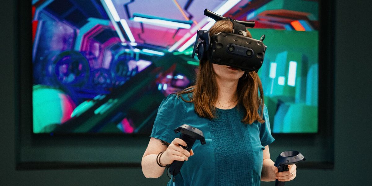 A person wearing a  virtual reality headset and holding hand controllers, walking on a specially designed platform called the omni deck in Helix, within the EC Stoner building.