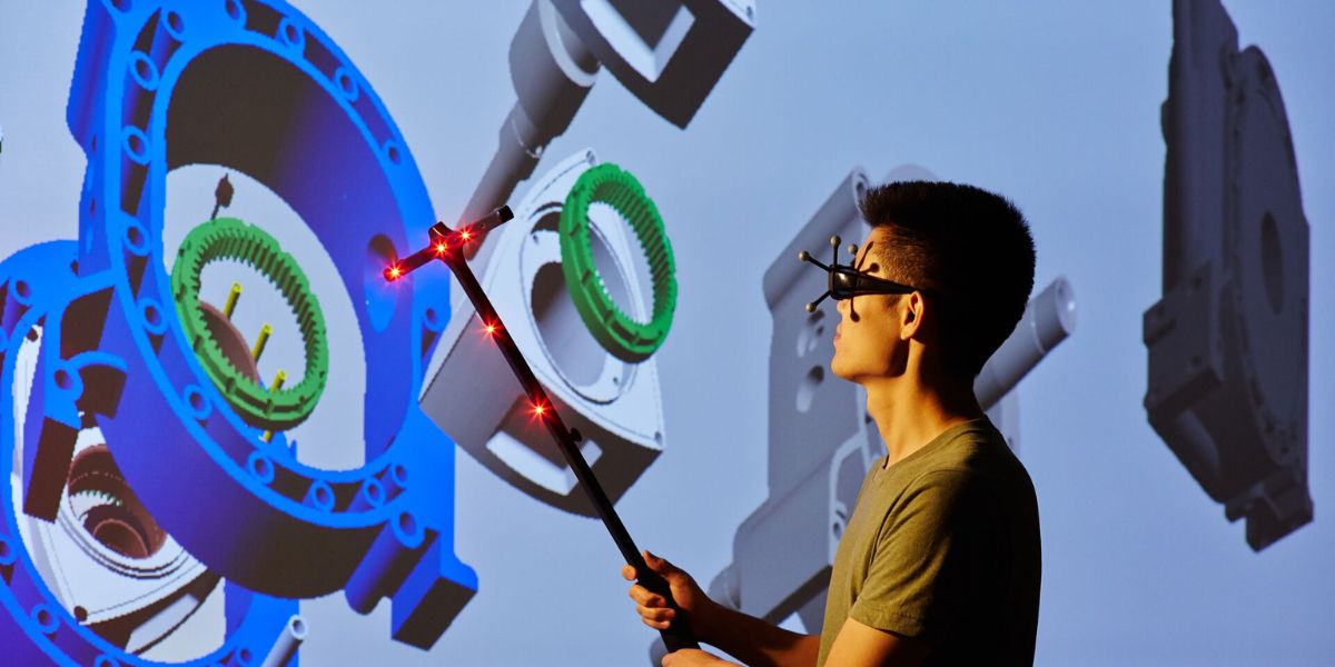 A student holding a t-shaped pole, which has red lasers, towards a wall that has large, green, blue and grey shapes projected onto it.