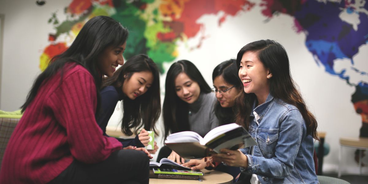 A group of students having a collaborative study session, smiling and discussing while sitting around a small table with open books.