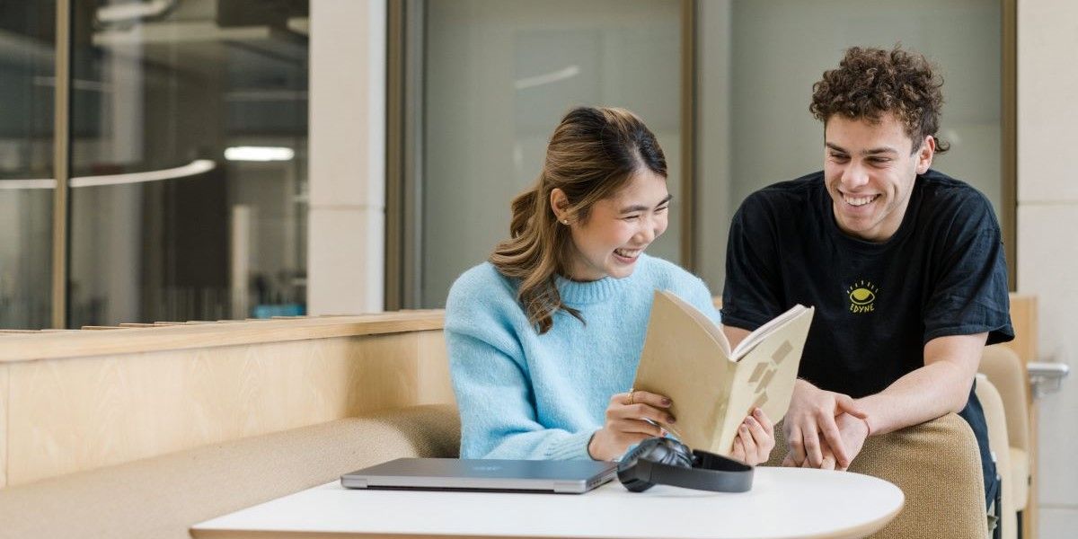 Two students smiling and looking at a book together.