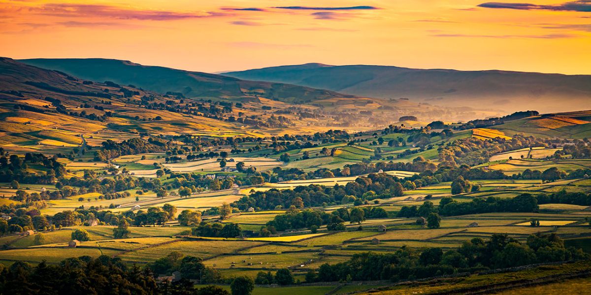 A valley in the Yorkshire Dales showing glowing sky, fields and rolling hills