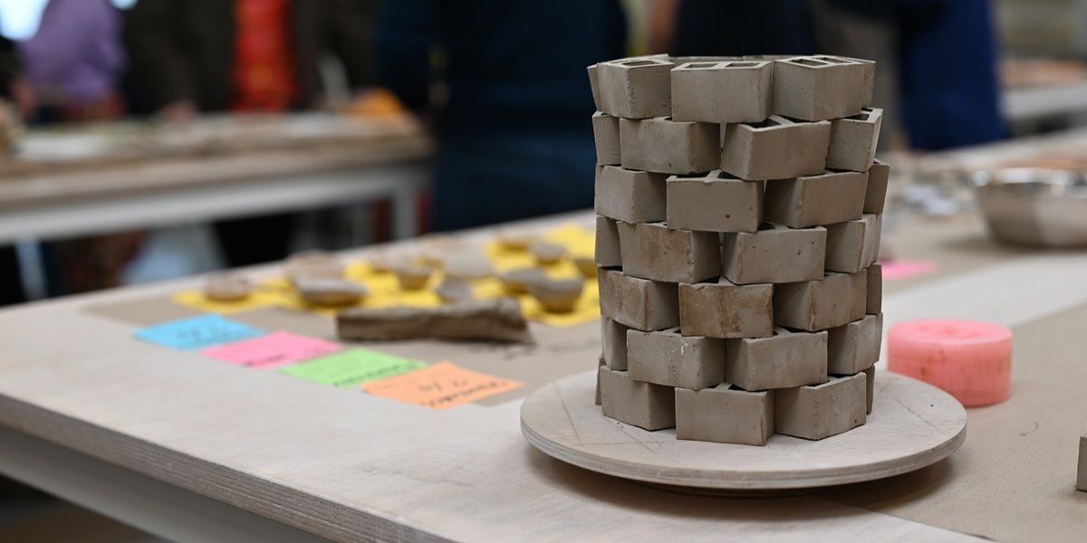 A small sculpture made of small clay bricks stacked on top of each other, on a desk in a workshop or studio