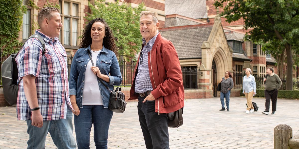 Three mature students, stood on campus smiling and chatting.