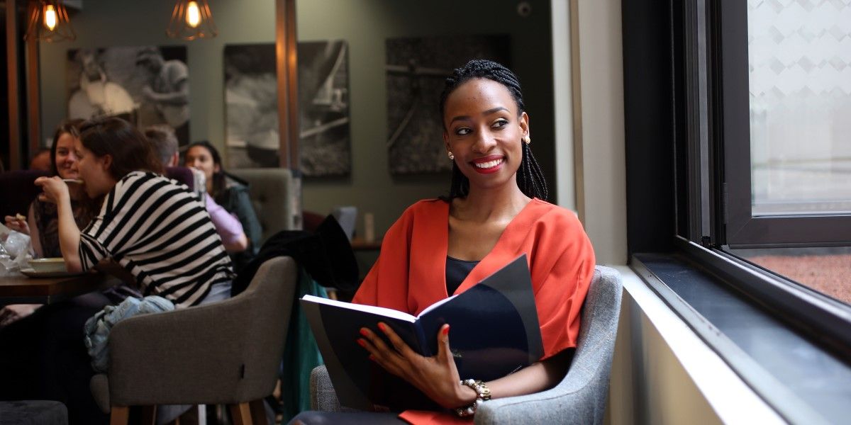 A person sitting in a cafe, holding open a large notebook and smiling.