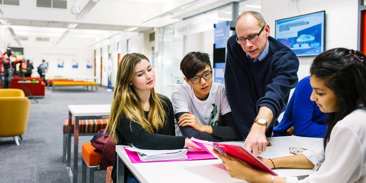 A group of students in a study space with a tutor who is chatting to them, discussing their work.