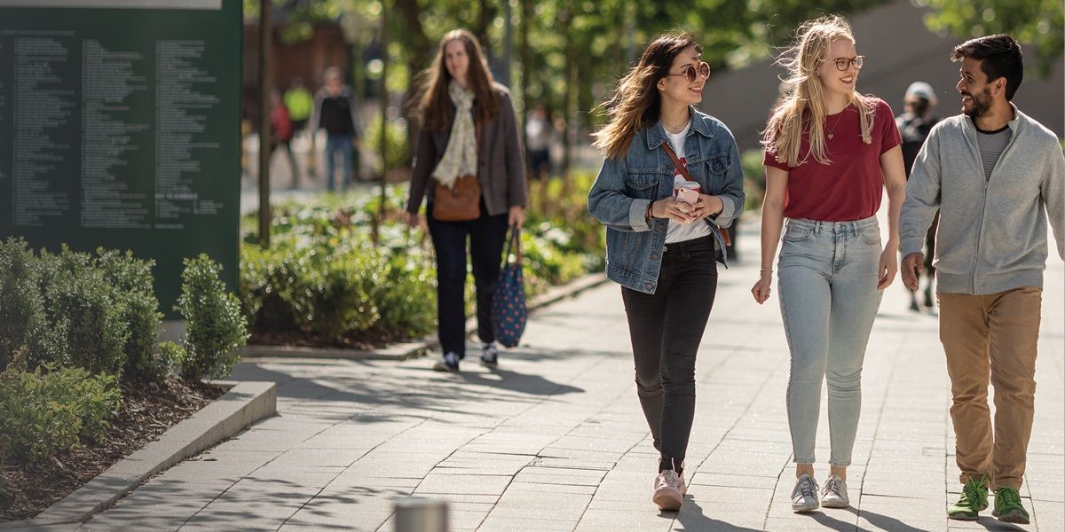 A group of three students walking on campus on a sunny day, chatting.