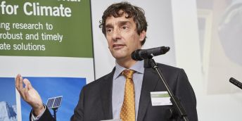 A head and shoulders shot of Professor Piers Forster stood behind a microphone on a stand.