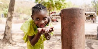 A smiling child drinks fresh water from a tap