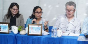 Dr Aarthi Bhuvaraghan (centre, holding microphone) and Professor John Walley seated at a table at a conference.