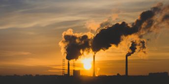 A picture of the setting sun, in the foreground chimneys emit fumes into the atmosphere