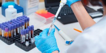 A person in a lab coat and blue gloves analyses a blood sample in a lab.