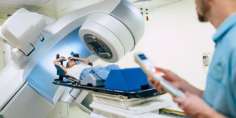 A patient undergoing radiotherapy. In the foreground, a radiologist holds a remote control for the linear accelerator machine.