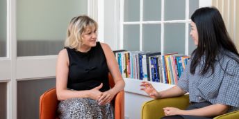Two colleagues chat on chairs with a row of books behind them
