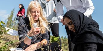 A young woman wearing a hijab and another woman in an outdoor setting, looking at grasses and plants.