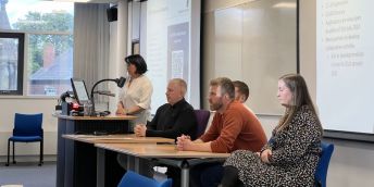 Five presenters on a panel, with one lasy standing and four people sitting, at a COIL event.
