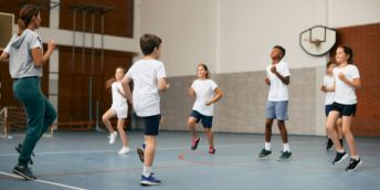 Children running on the spot in a sports hall, accompanied by a teacher