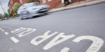 White paint on a tarmacked road spelling out the words Car Club. There is a silver car driving by in the background