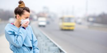Person wearing face mask standing beside a busy road which is foggy with air pollution