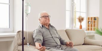 Elderly person, hooked up to an IV drip, sitting on a sofa