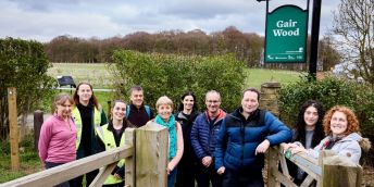 Nick Plant is leaning on the gate marking the entrance to the new pathway across Gair Wood site. He is surrounded by volunteers called Friends of Gair Wood.