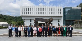 Members of the World Universities Network are gathered in a line in front of a concrete building and a sculpture.
