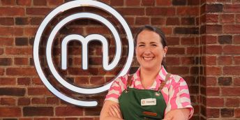 Frankie Dunn stands in an apron in from of the MasterChef logo