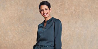Naga Munchetty, wearing a grey dress, smiles at the camera in front of a beige background