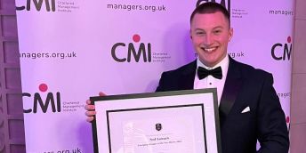 Ned Samuels is stood holding his  framed award in front of a Chartered Management Institute banner.