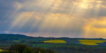 Sunlight breaking through storm clouds above a rural landscape.
