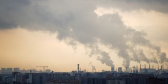 A cityscape with several chimneys pumping out smoke into the atmosphere