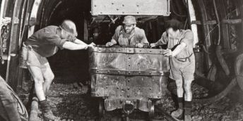 a black and white photograph of three men pushing a mine cart