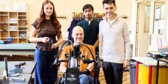 Ava and Swayam with their client Nick who is on his bike and Alex Sobel MP stood in a workshop in the School of Mechanical Engineering.