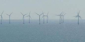 The images shows an offshore windfarm on a calm  day. The sea is flat.
