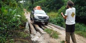 A four by four vehicle carrying equipment into the Amazon over a narrow bridge made of logs.