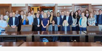 A large group of people sat and stood around a table.