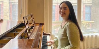 Sophie Lim smiles at the camera whilst playing the piano at Leeds City Museum