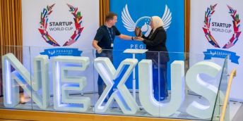 Gareth Scargill presents the winners trophy to Rania Maklad with the Nexus logo in front and Startup world cup banners in the background.