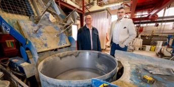 Two researchers stand behind concrete-mixing equipment in large engineering lab.