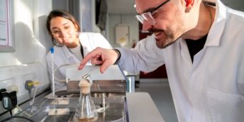 Professor Nik Watson looks at a conical flask with a student.