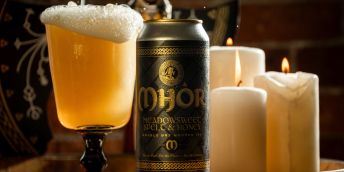 Dramatic shot of a cup of beer, the Northern Monk Mhór can and three candles