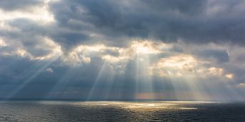 The sun breaks through the clouds and shines on the ocean.