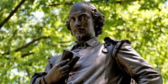 A statue of William Shakespeare viewed from below with greenery in the background