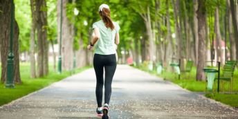 A sole woman in a green and black sportswear running through a park