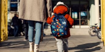 a rear view of a parent and a young child arriving outside a school