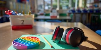 A desk with a fidget toy, a pencil and some ear defenders on it