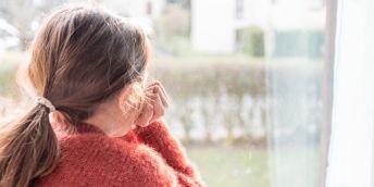 A child with long hair looking out of the window with their chin reasting on their hand
