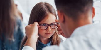 A person placing a pair of glasses on a child's face